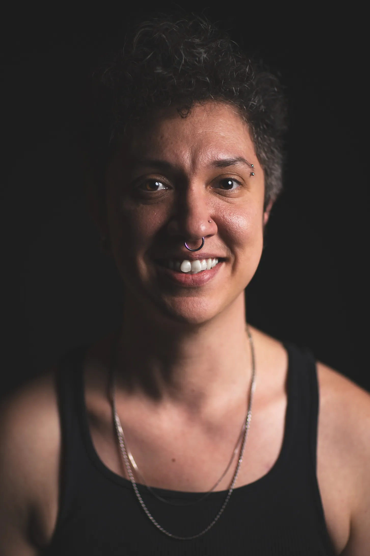 A portrait of Fox Moon, the massage therapist, as they smile in front of a black background.