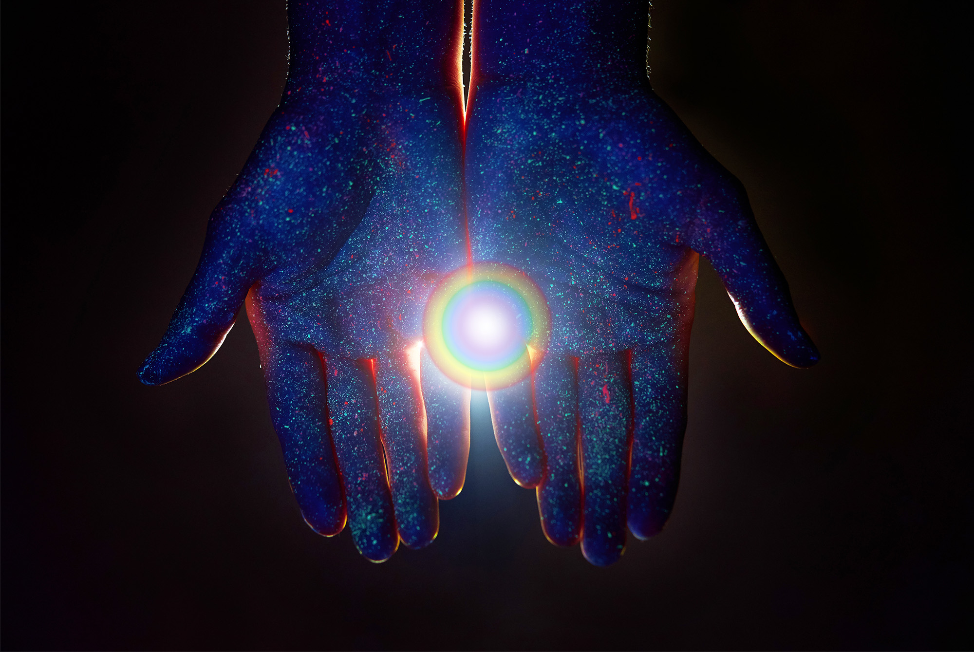 The palms of two cupped hands with a beam of rainbow prism shining  out of them.